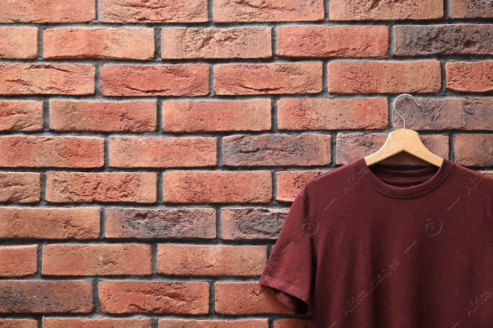 Photo of Hanger with brown t-shirt against red brick wall, closeup. Mockup for design