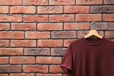 Photo of Hanger with brown t-shirt against red brick wall, closeup. Mockup for design