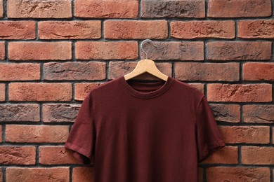 Photo of Hanger with brown t-shirt against red brick wall, closeup. Mockup for design
