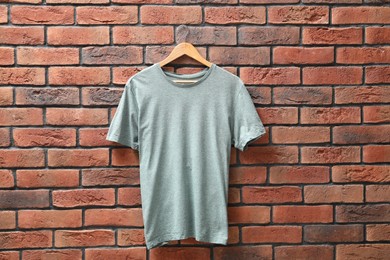 Photo of Hanger with gray t-shirt against red brick wall. Mockup for design