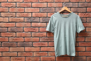 Photo of Hanger with gray t-shirt against red brick wall. Mockup for design