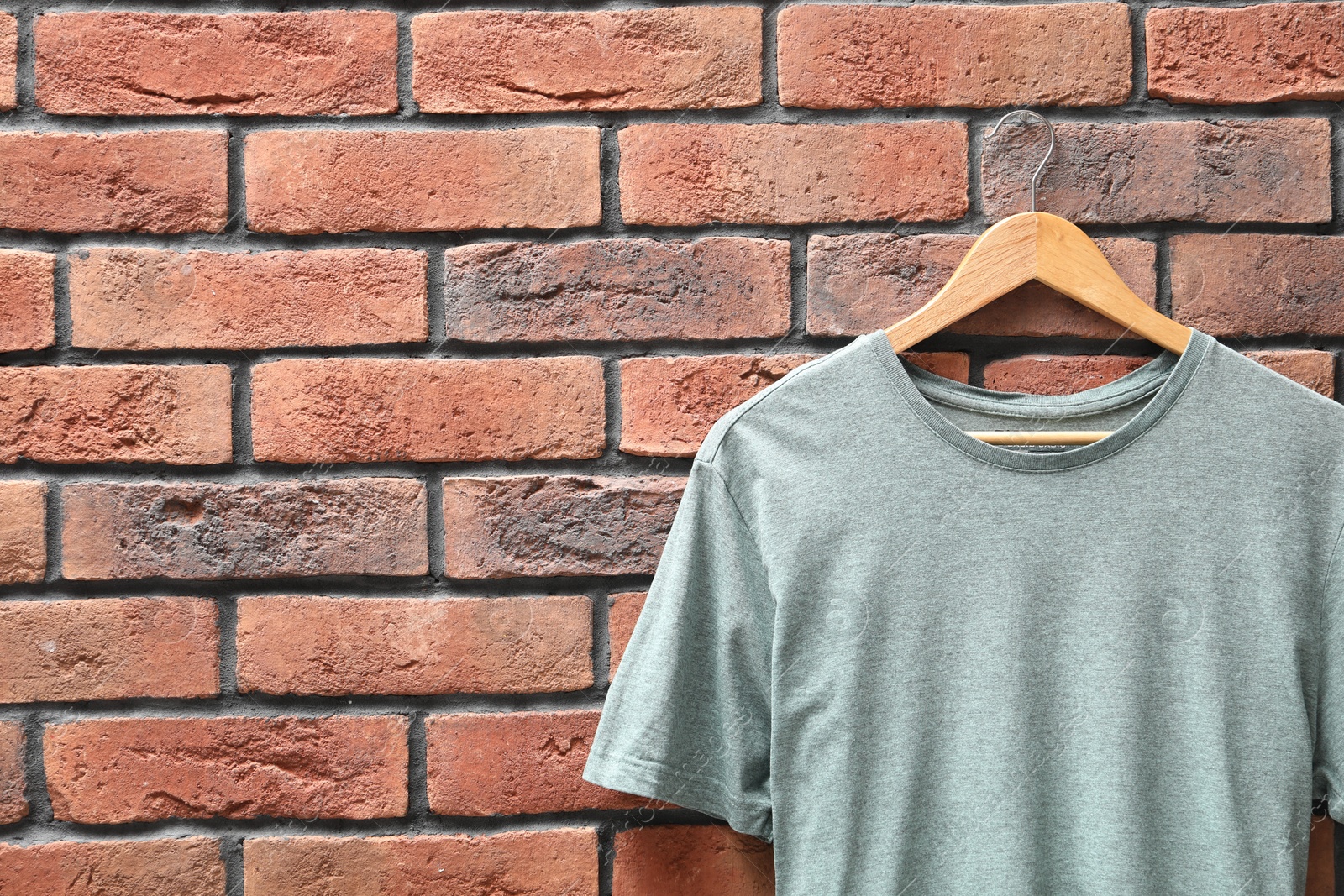 Photo of Hanger with gray t-shirt against red brick wall, closeup. Mockup for design