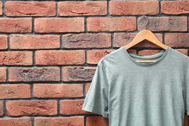 Photo of Hanger with gray t-shirt against red brick wall, closeup. Mockup for design