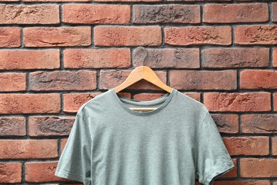 Photo of Hanger with gray t-shirt against red brick wall, closeup. Mockup for design