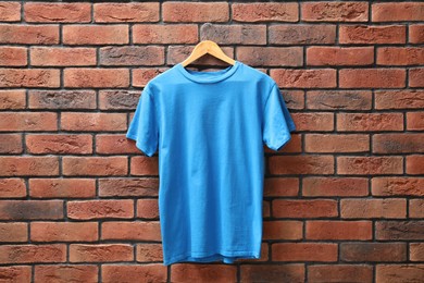 Photo of Hanger with light blue t-shirt against red brick wall. Mockup for design