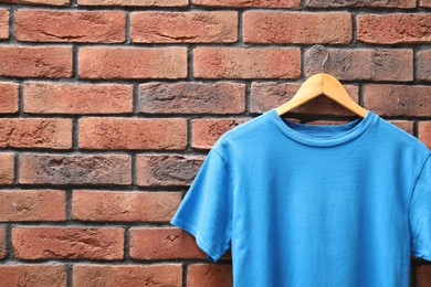 Photo of Hanger with light blue t-shirt against red brick wall, closeup. Mockup for design