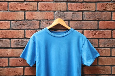 Photo of Hanger with light blue t-shirt against red brick wall, closeup. Mockup for design