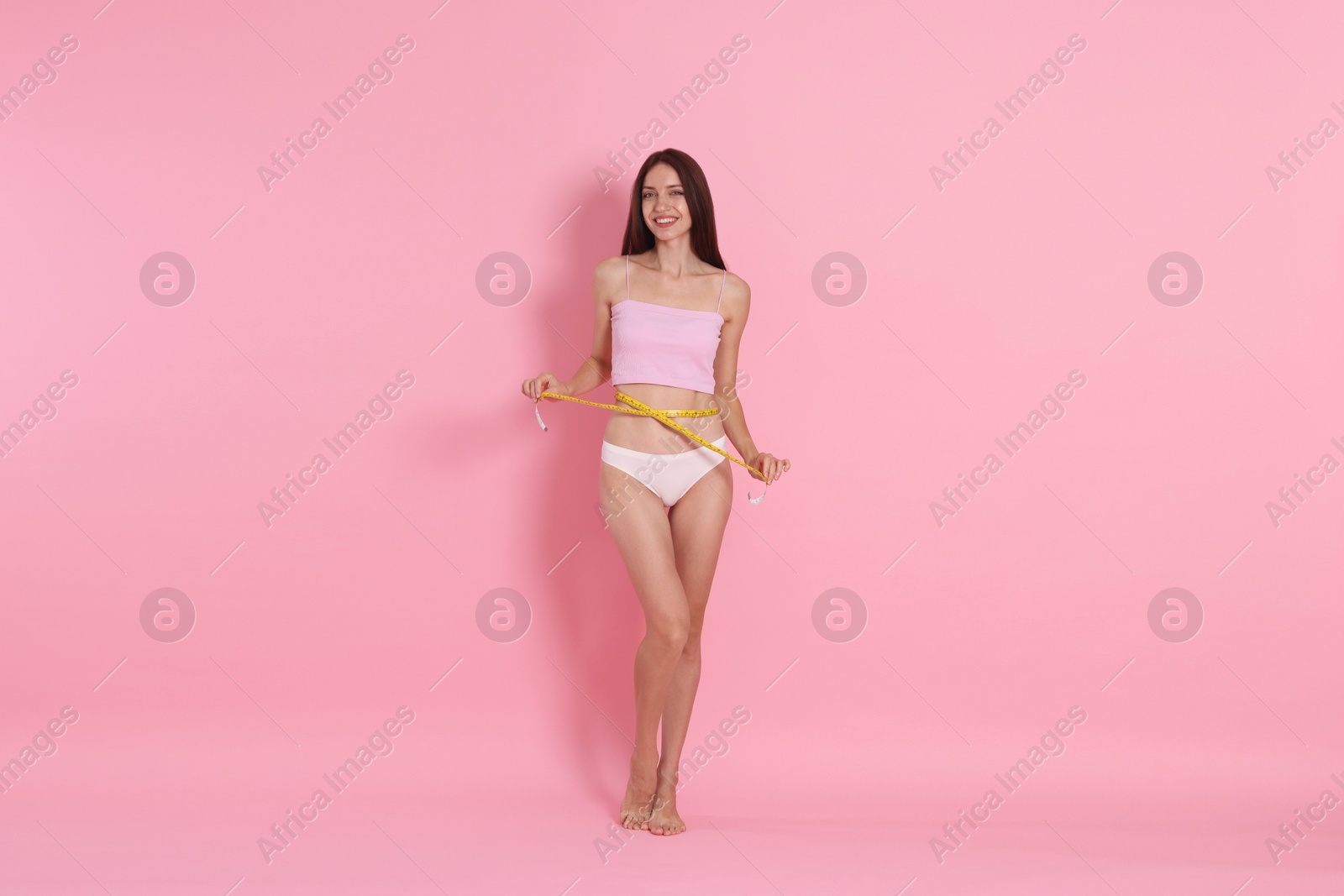 Photo of Woman with slim body measuring waist circumference on pink background