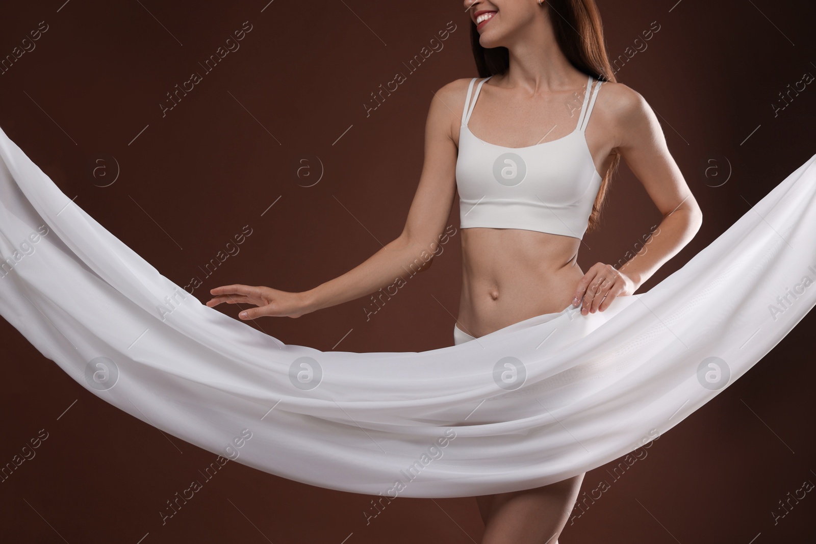Photo of Woman covering her slim body with silk fabric on brown background, closeup
