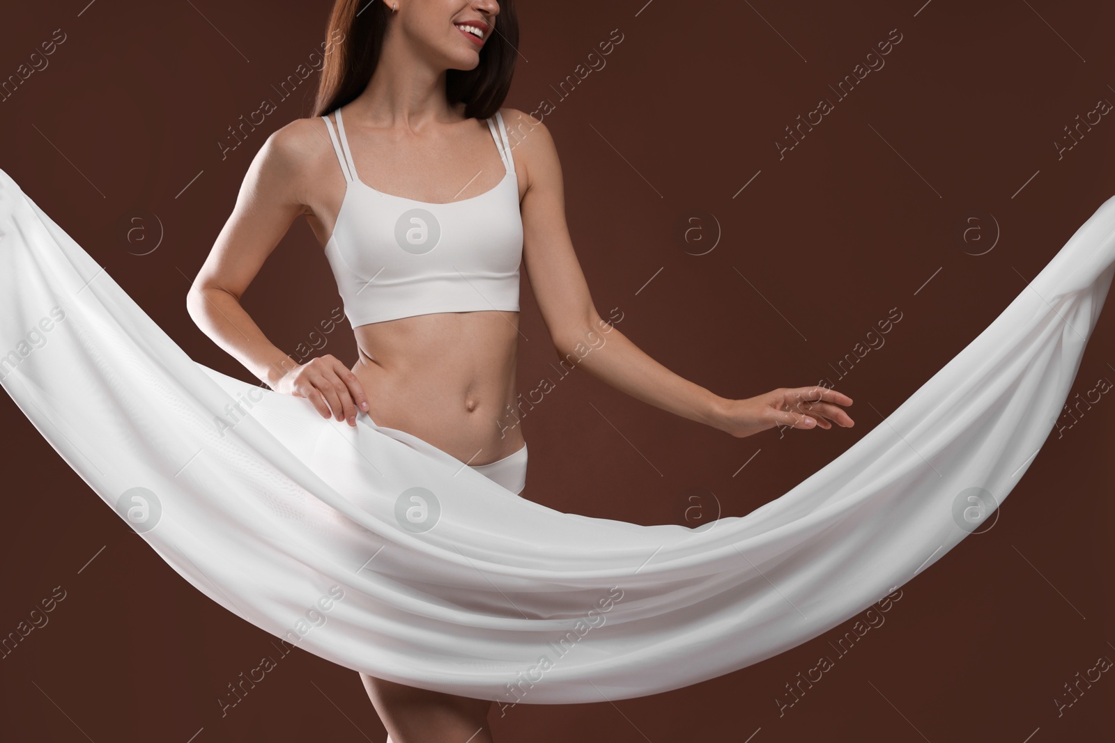 Photo of Woman covering her slim body with silk fabric on brown background, closeup