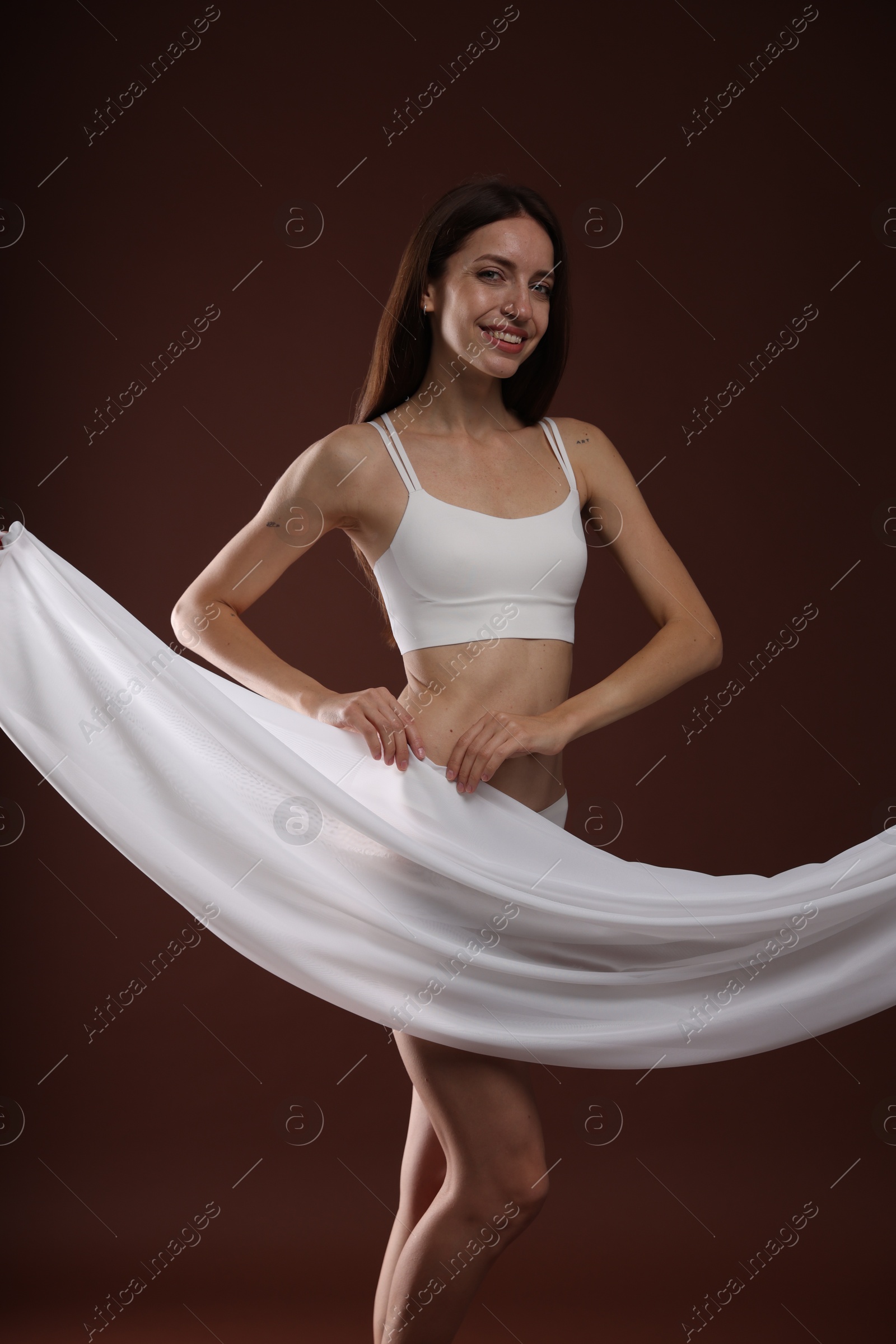 Photo of Woman covering her slim body with silk fabric on brown background