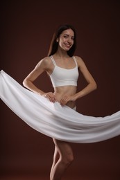 Photo of Woman covering her slim body with silk fabric on brown background