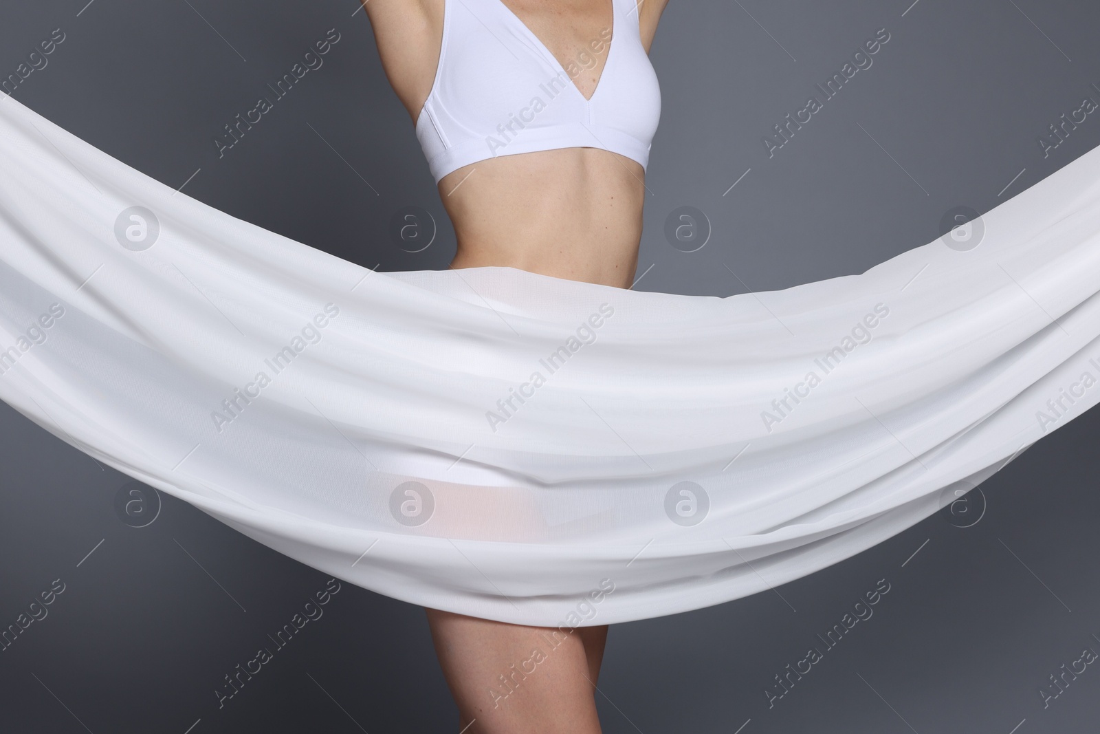 Photo of Woman covering her slim body with silk fabric on grey background, closeup