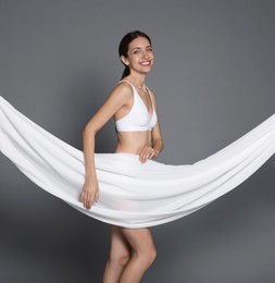 Photo of Woman covering her slim body with silk fabric on grey background
