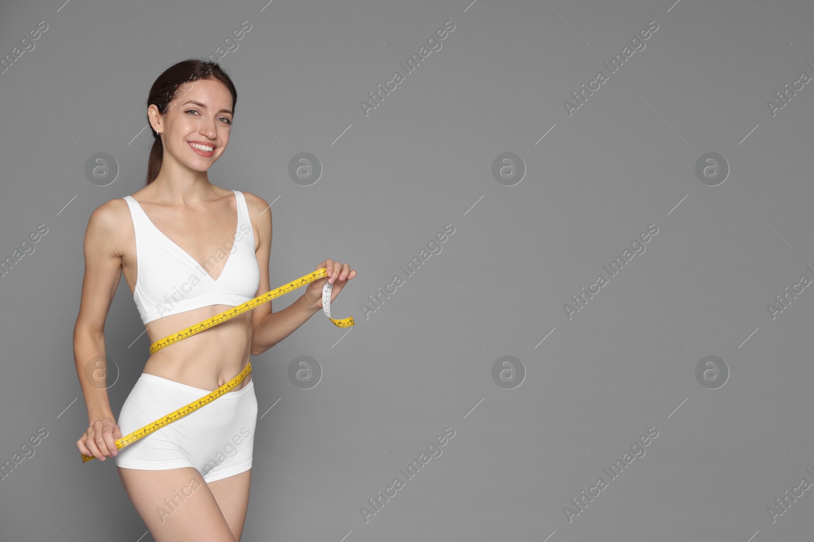 Photo of Woman with slim body and measuring tape on grey background, space for text