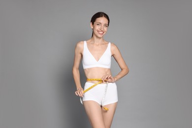 Photo of Woman with slim body measuring waist circumference on grey background