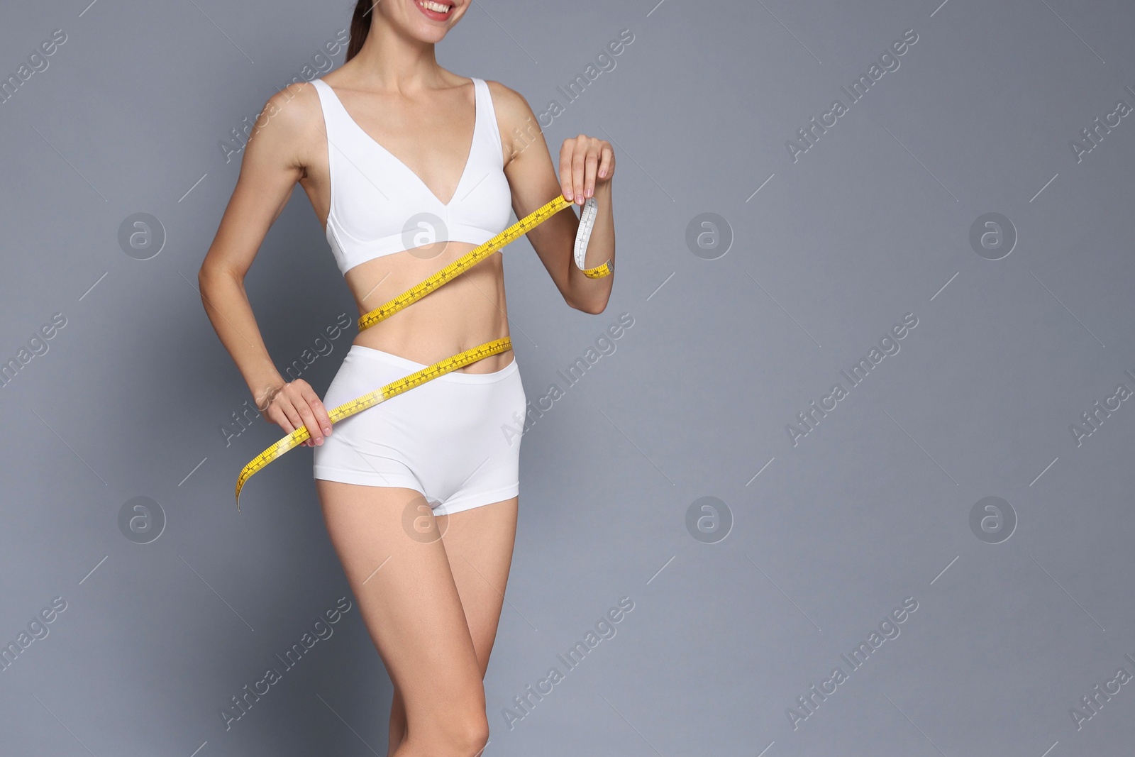 Photo of Woman with slim body and measuring tape on grey background, closeup. Space for text