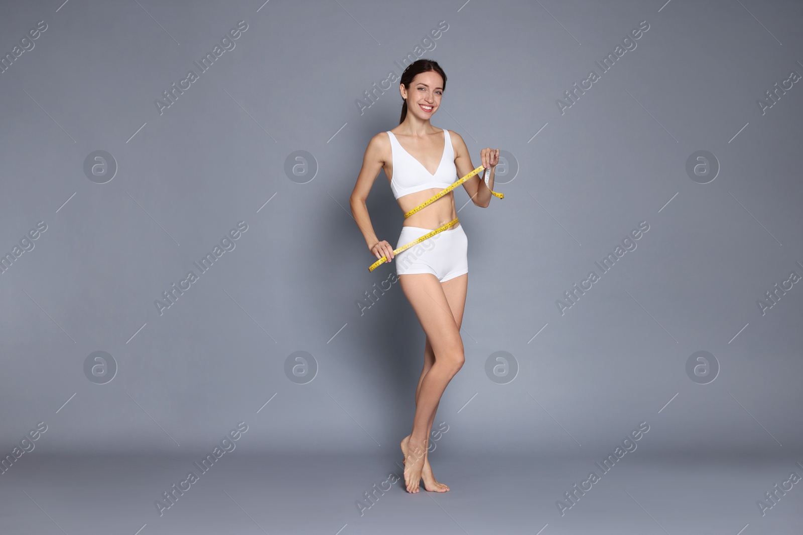 Photo of Woman with slim body and measuring tape on grey background