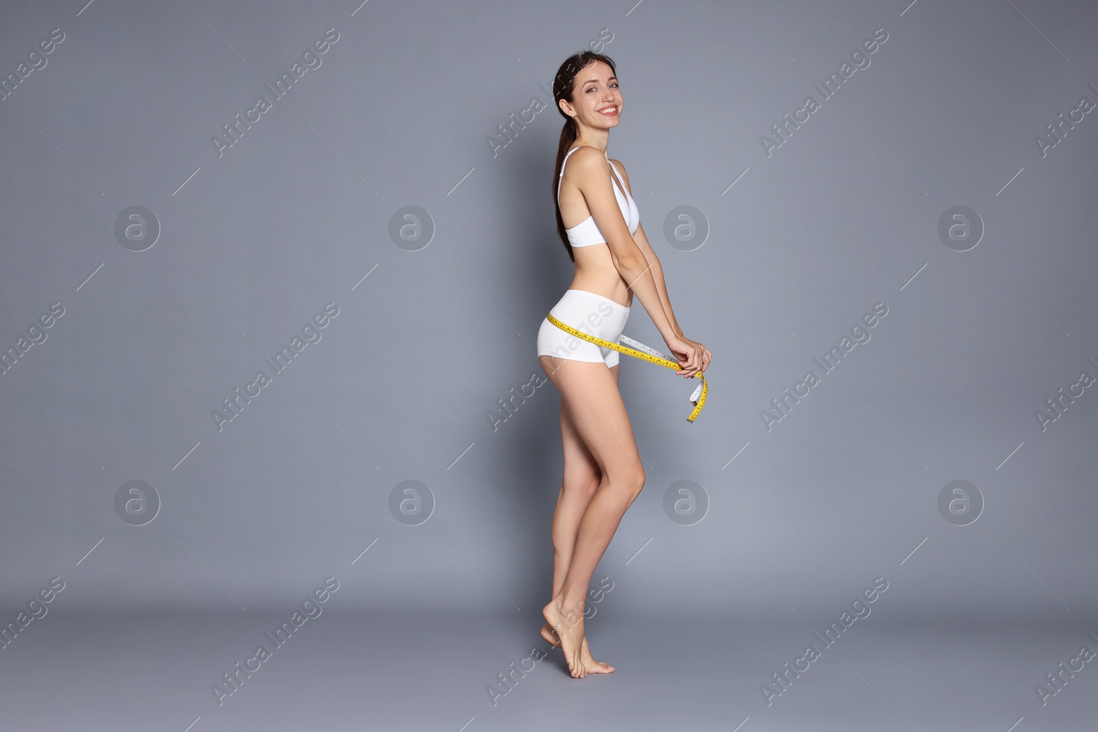 Photo of Woman with slim body and measuring tape on grey background