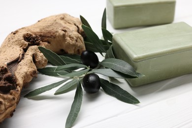 Photo of Handmade soap bars, olives, snag and green leaves on white wooden table, closeup