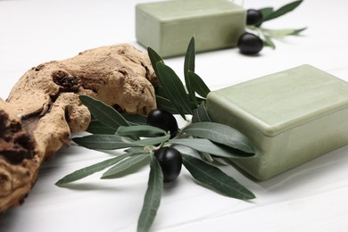 Photo of Handmade soap bars, olives, snag and green leaves on white wooden table, closeup