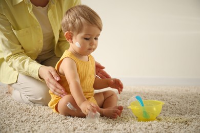 Photo of Cute baby with cream on his body playing with mom at home, closeup. Space for text