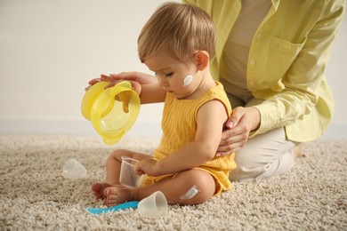 Photo of Cute baby with cream on his body playing with mom at home, closeup