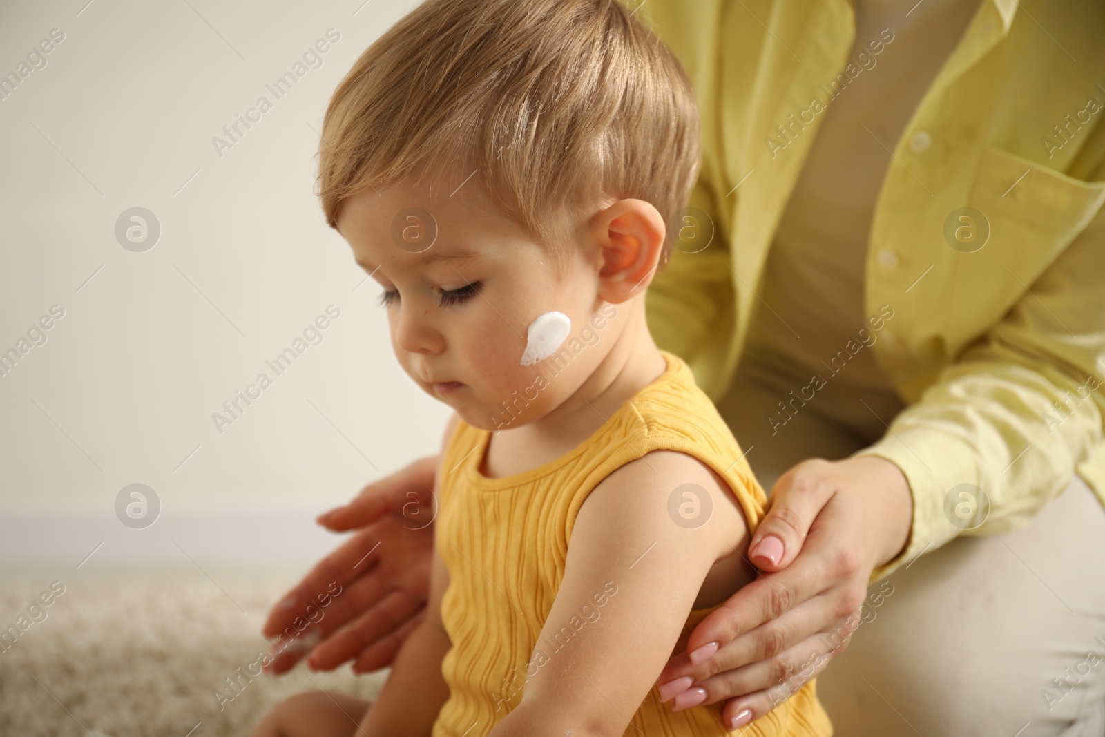 Photo of Cute baby with cream on his body playing with mom at home, closeup