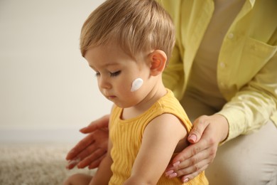 Photo of Cute baby with cream on his body playing with mom at home, closeup