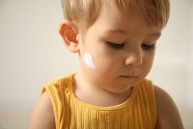 Photo of Cute baby with cream on his face at home, closeup
