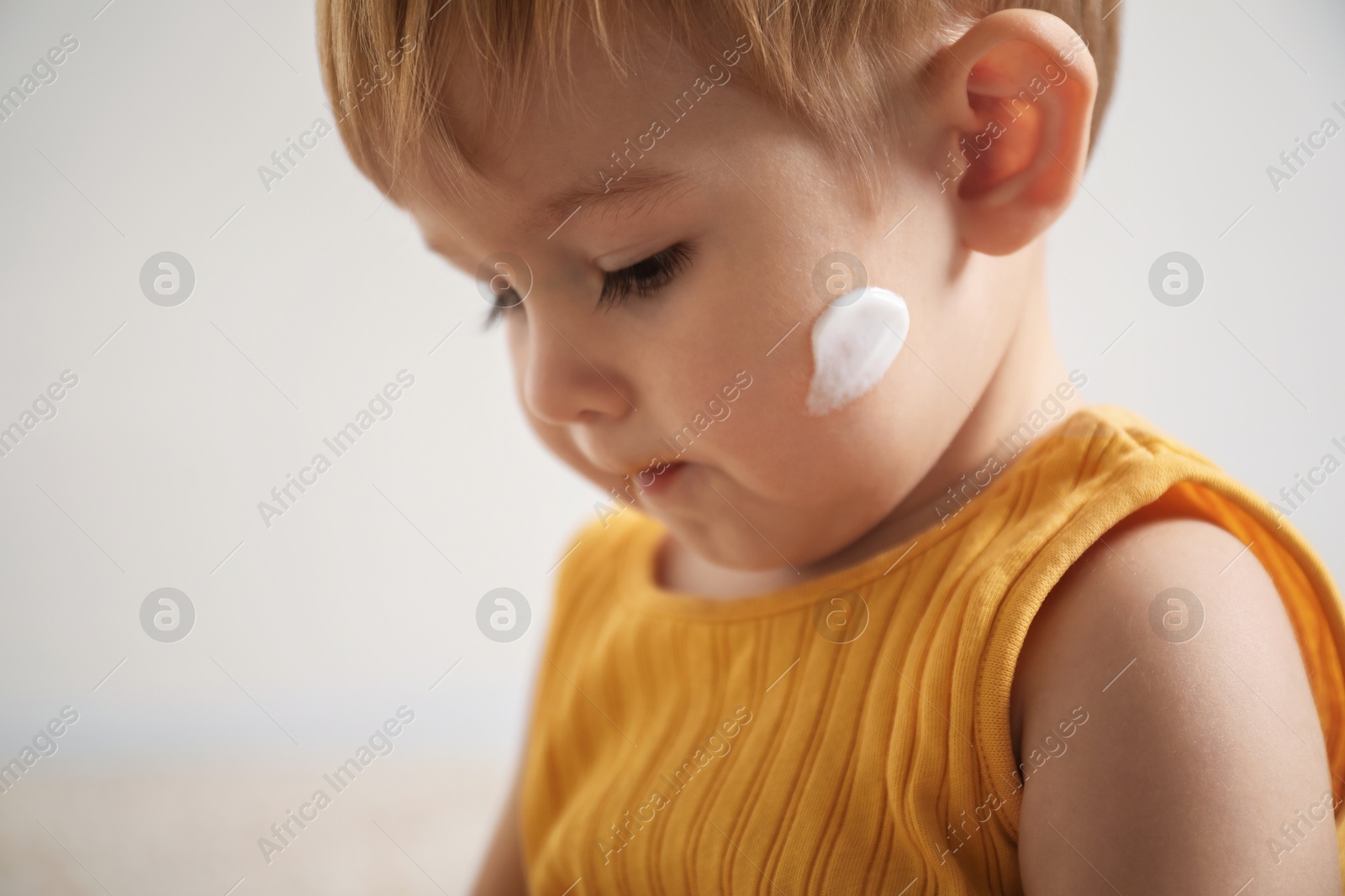 Photo of Cute baby with cream on his face at home, closeup