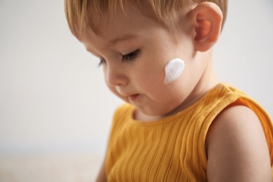 Photo of Cute baby with cream on his face at home, closeup
