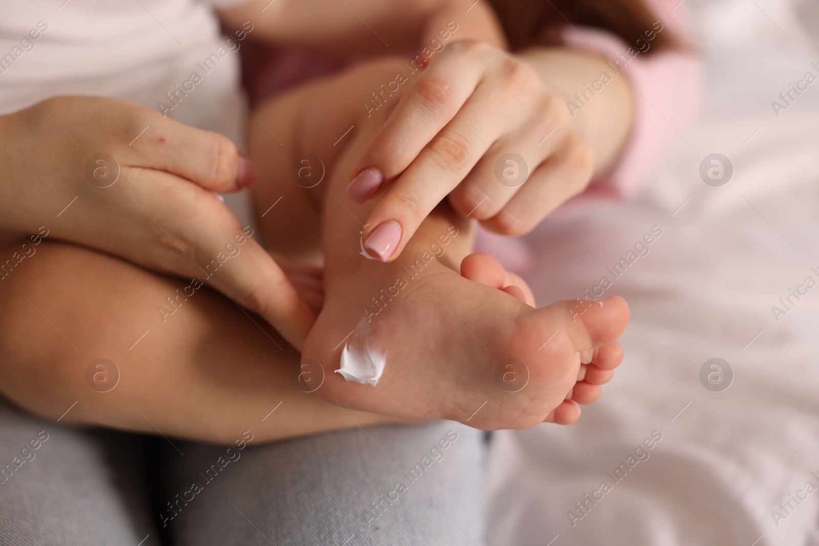 Photo of Mother applying cream onto her baby's foot at home, closeup