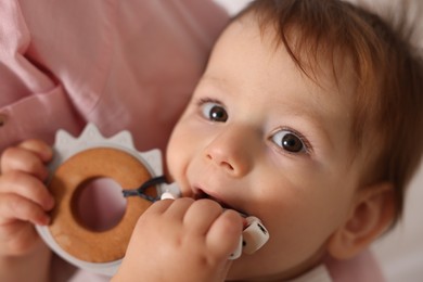 Photo of Mother with her cute baby biting teether toy at home, closeup