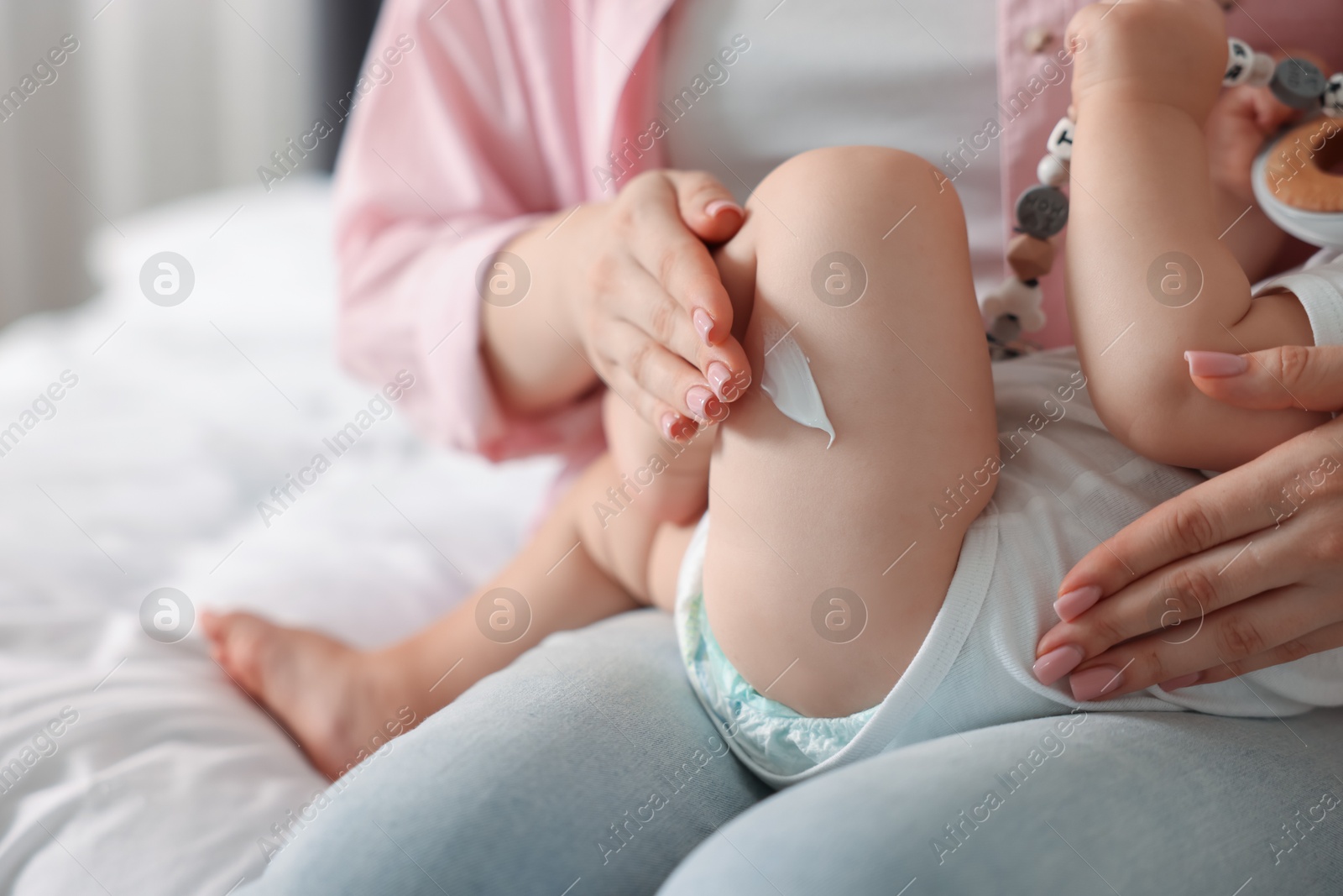 Photo of Mother applying cream onto her baby's leg at home, closeup