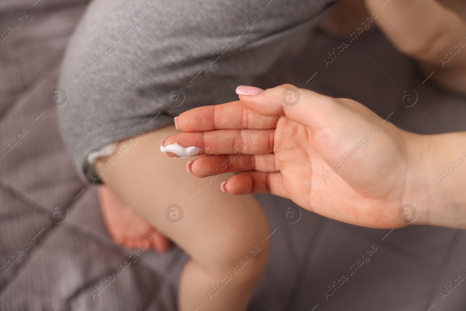 Photo of Mother applying cream onto her baby's body at home, closeup