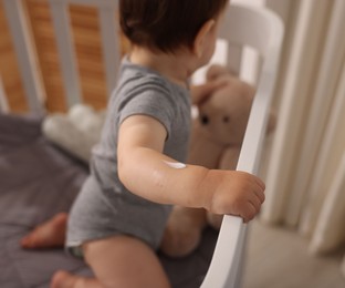 Photo of Baby with cream on his arm in crib at home, closeup