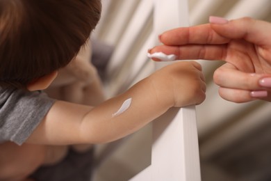 Photo of Mother applying cream onto her baby's arm at home, closeup