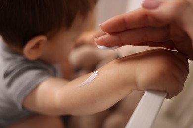Photo of Mother applying cream onto her baby's arm at home, closeup