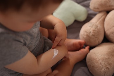 Photo of Baby with cream on his arm in crib at home, closeup