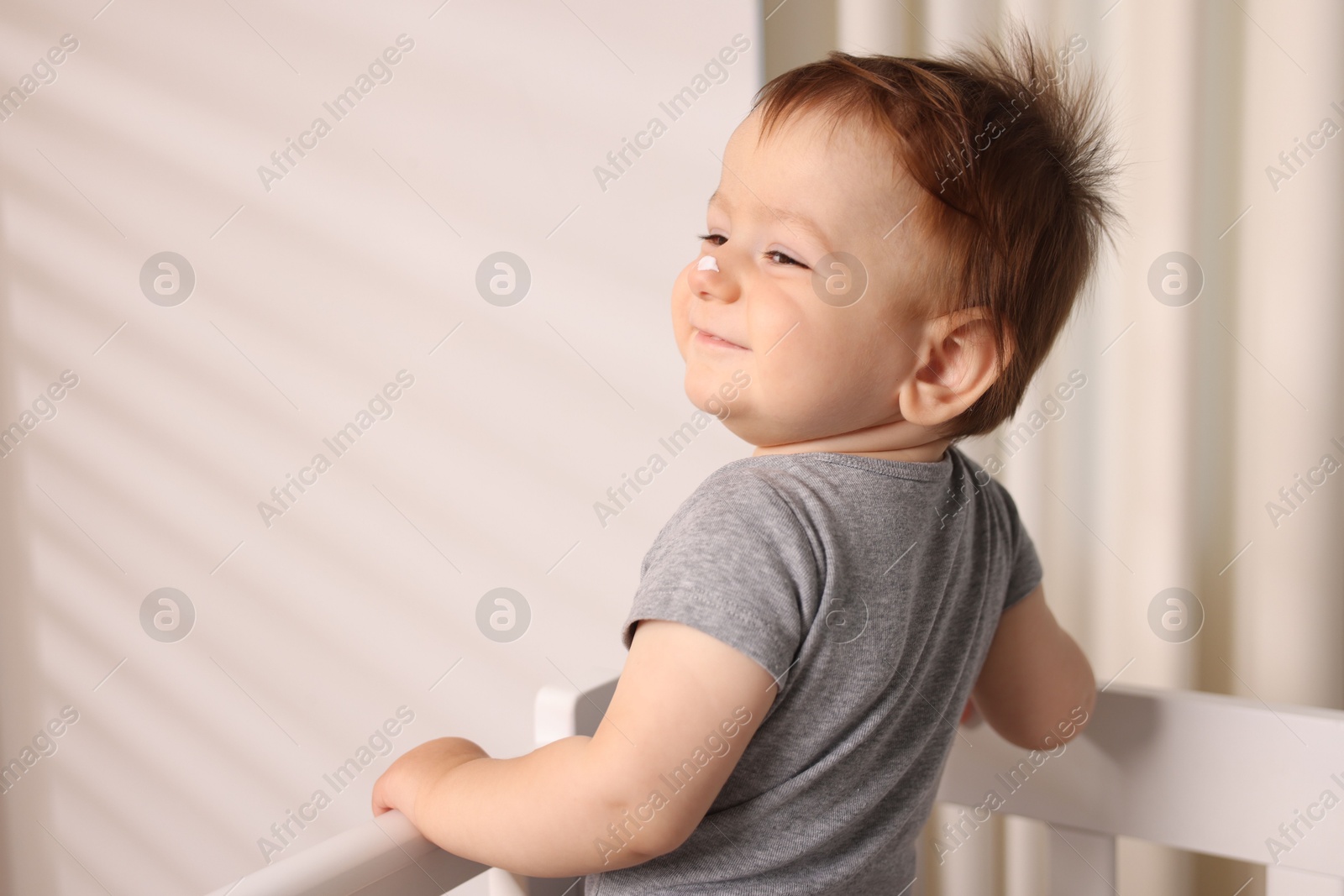Photo of Baby with cream on his nose in crib at home. Space for text