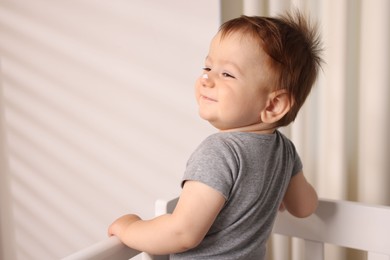 Photo of Baby with cream on his nose in crib at home. Space for text
