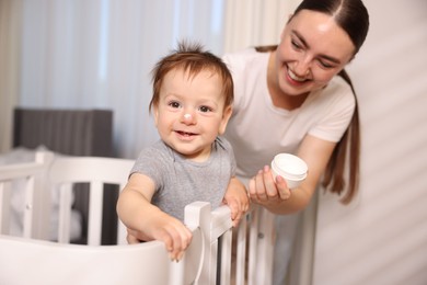 Photo of Mother and baby with cream on his nose at home, selective focus