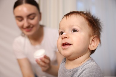 Photo of Mother and baby with cream on his nose at home, selective focus