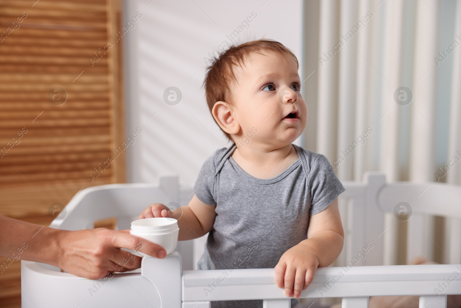 Photo of Mother with jar of cream and her baby in crib at home, closeup