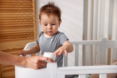 Photo of Mother with jar of cream and her baby in crib at home, closeup