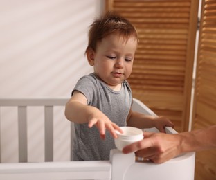 Photo of Mother with jar of cream and her baby in crib at home, closeup