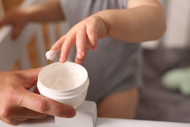 Photo of Mother with jar of cream and her baby in crib at home, closeup