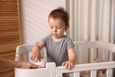 Photo of Mother with jar of cream and her baby in crib at home, closeup