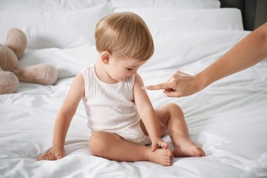 Photo of Mother applying cream onto her baby's arm on bed at home, closeup
